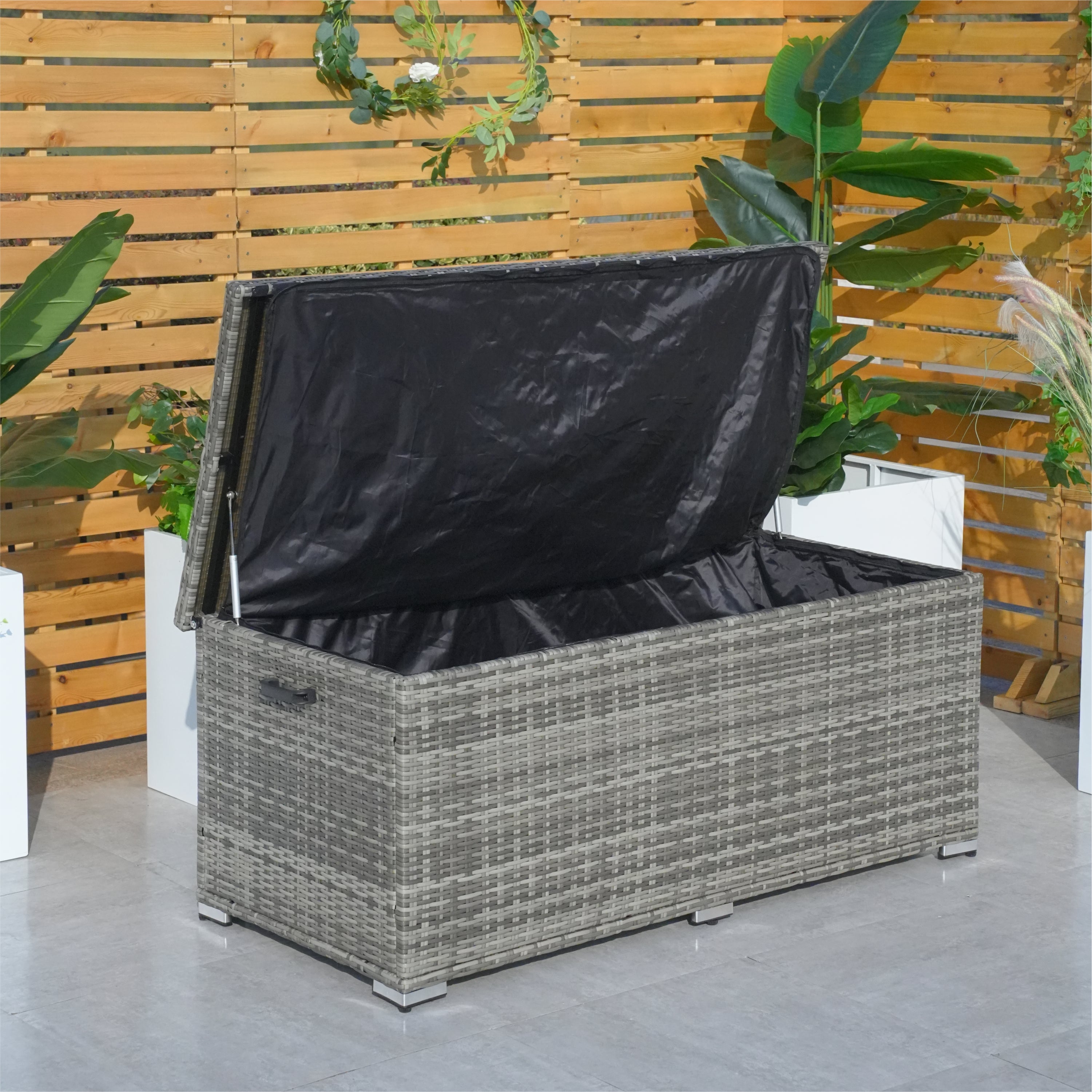 A compact aluminium rattan storage box with a black waterproof cover, placed on a patio between two potted plants.