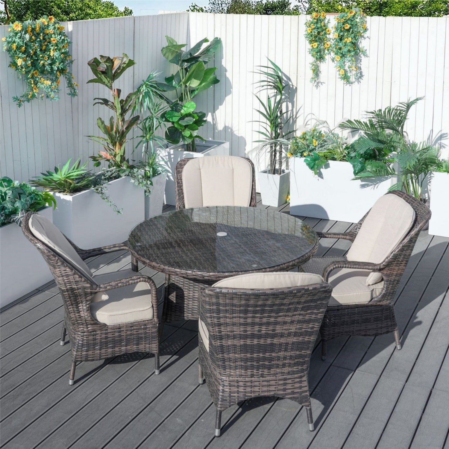 A Parma 4-Seat Outdoor Dining Set with a round table and four chairs with cushions, placed on a deck surrounded by green plants.