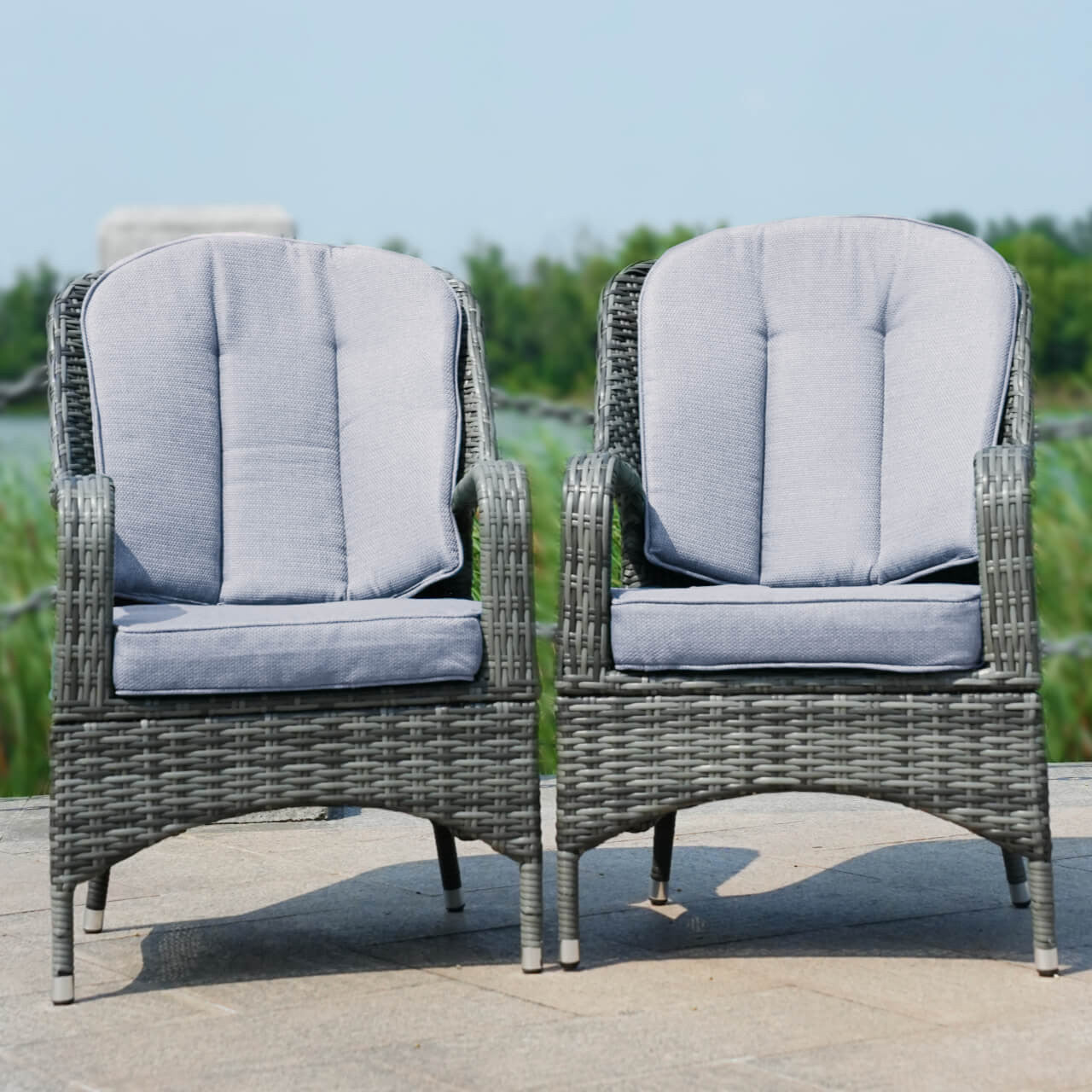 Two brown aluminum rattan armchairs with thick cushions placed outdoors, likely on a patio or garden setting.