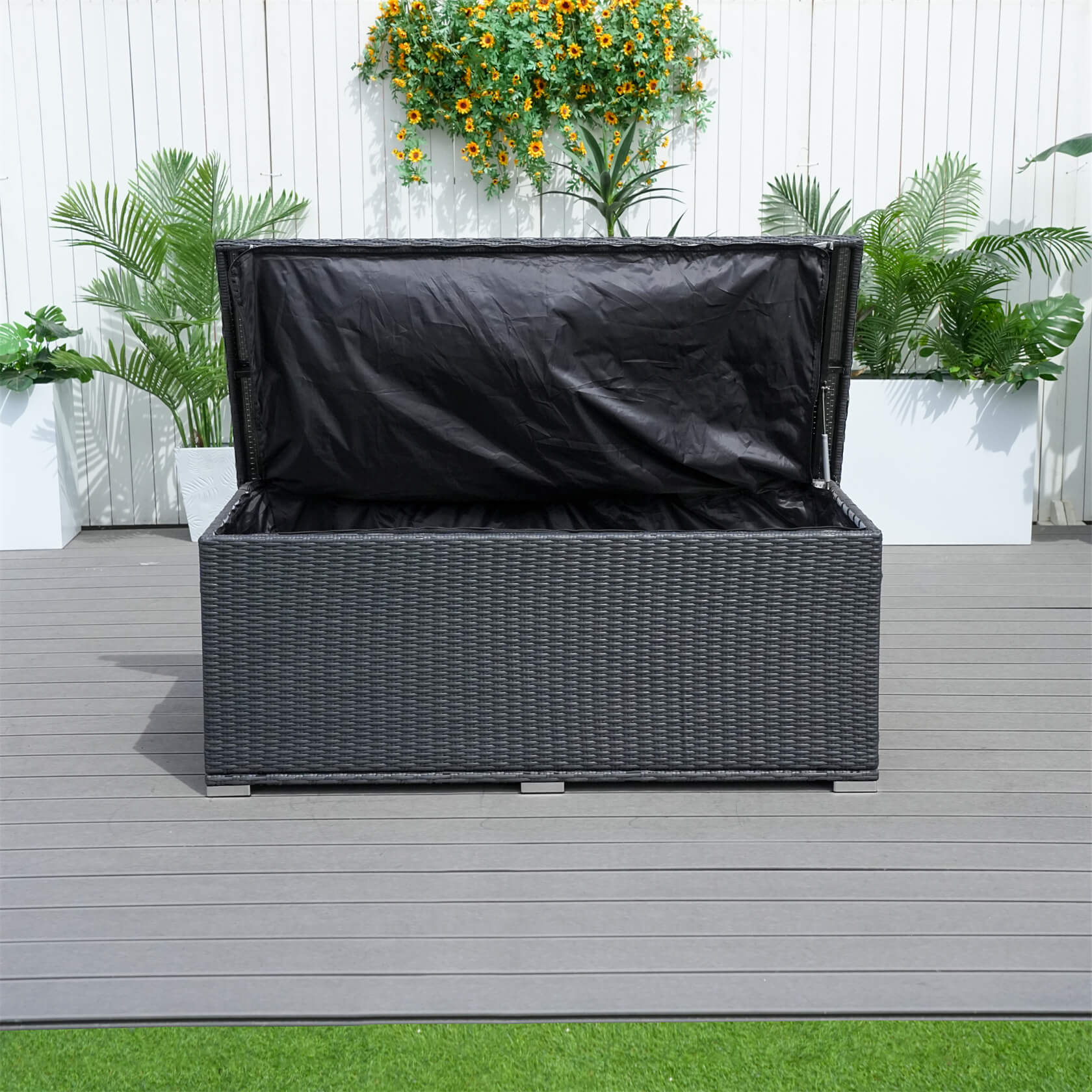 black wicker storage box with a black cover on a wooden deck with plants in the background