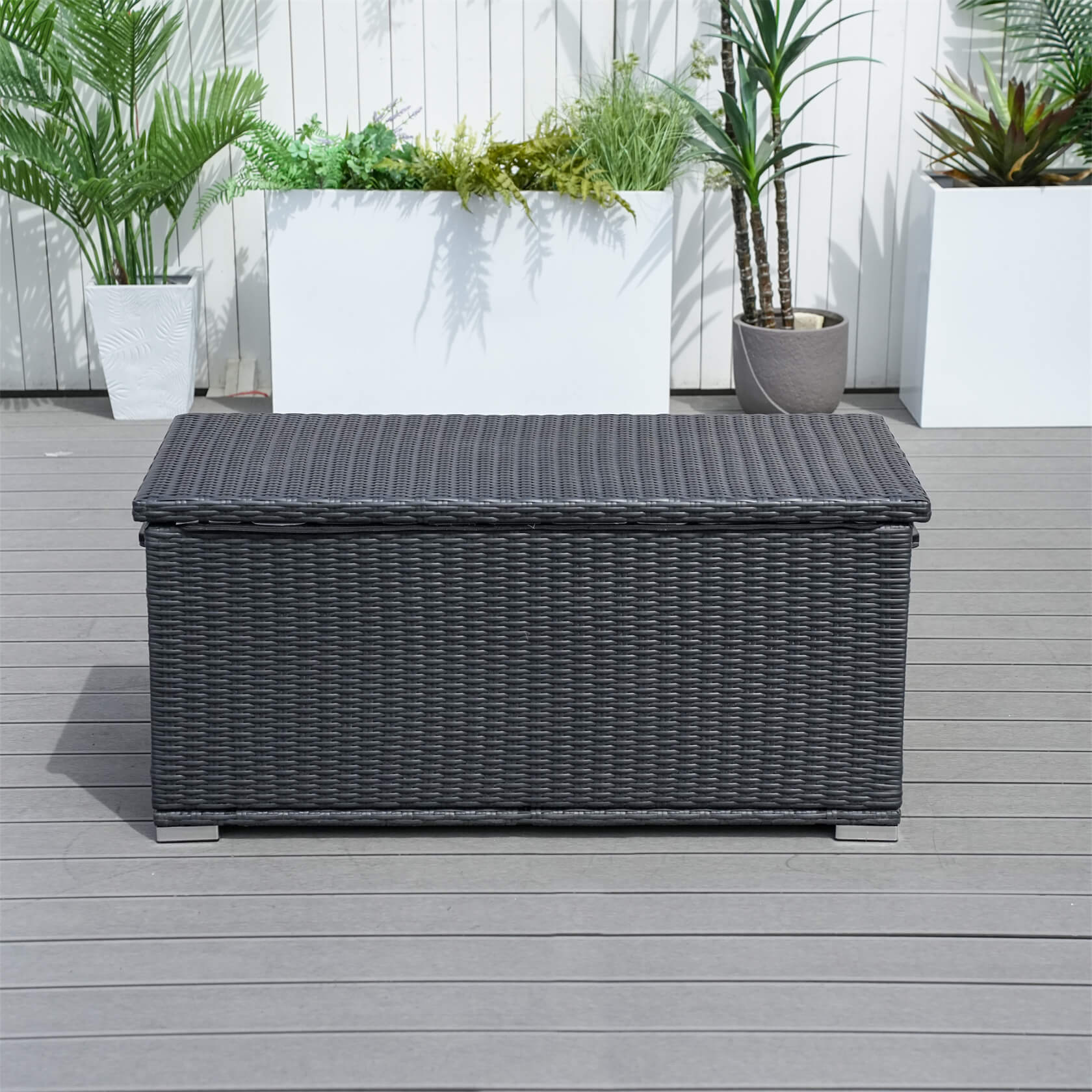 Black wicker storage box on a wooden deck with plants in the background